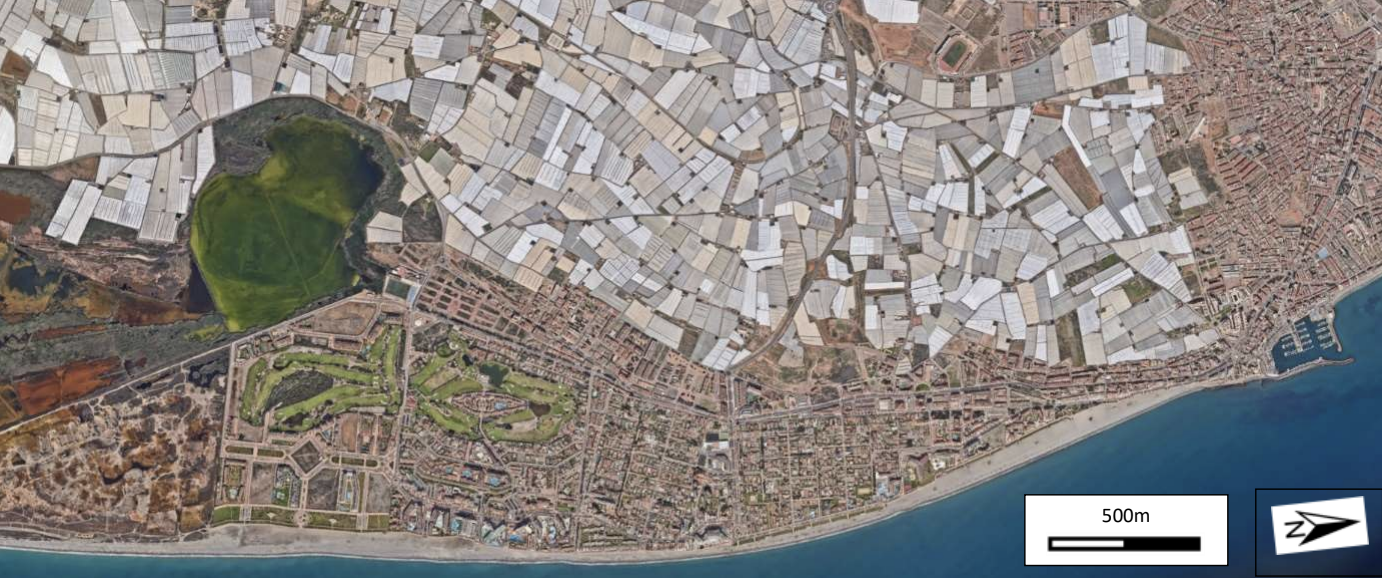 Luftbild einer Küstenstadt mit Strand, Häusern, Gewächshausfeldern und Yachthafen